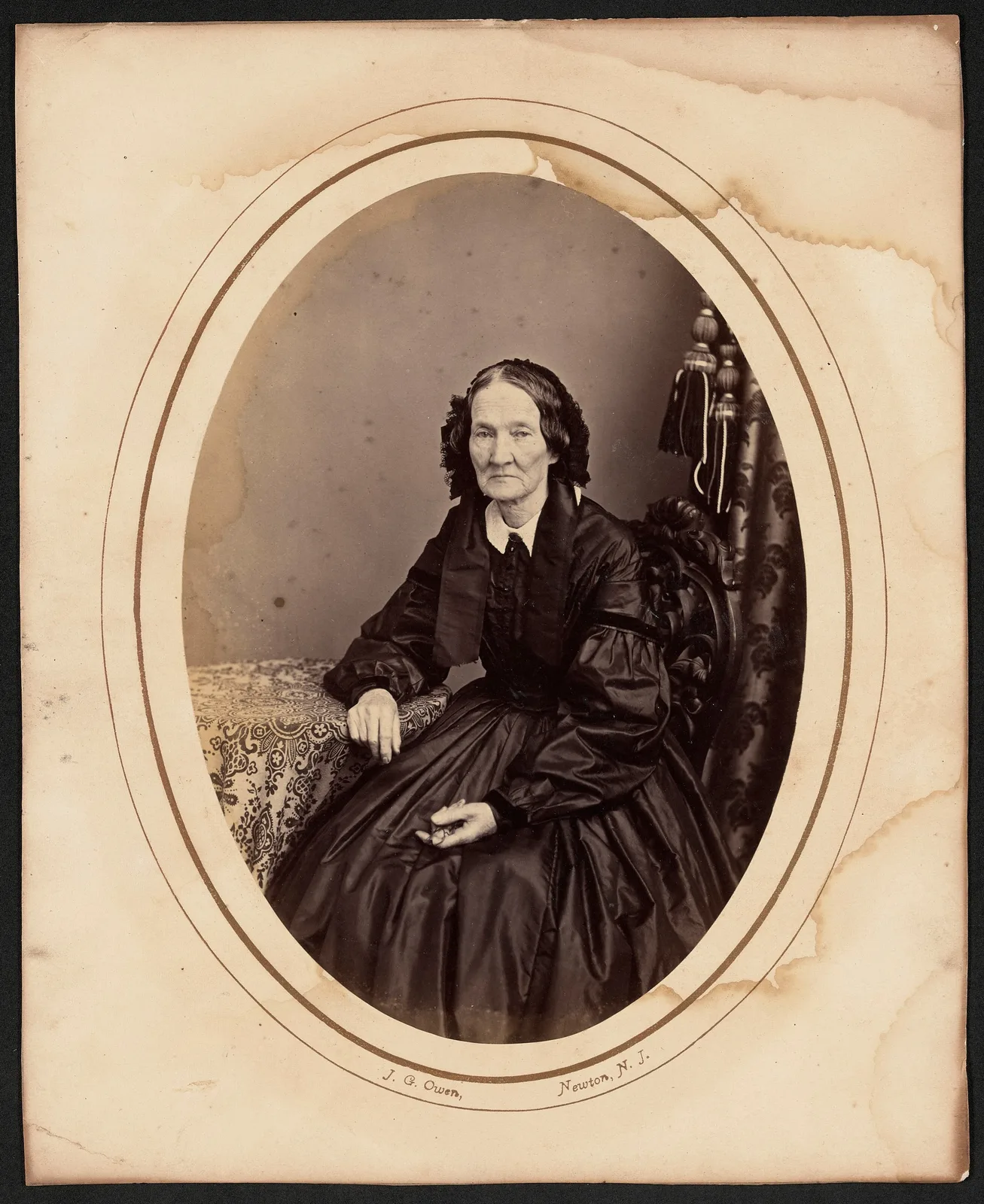 Original: An elderly woman in a black dress, oval-matted portrait with stains