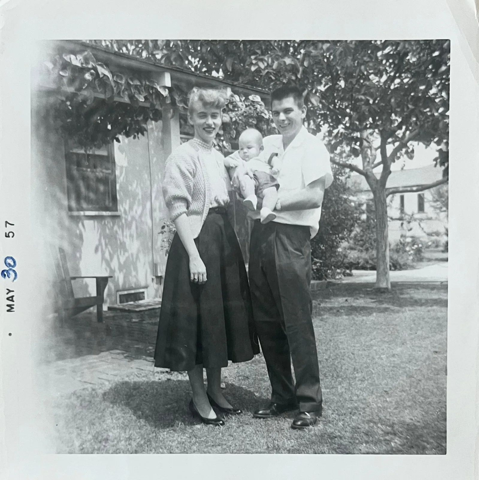 Original: A young couple holding their baby in a garden, May 1957