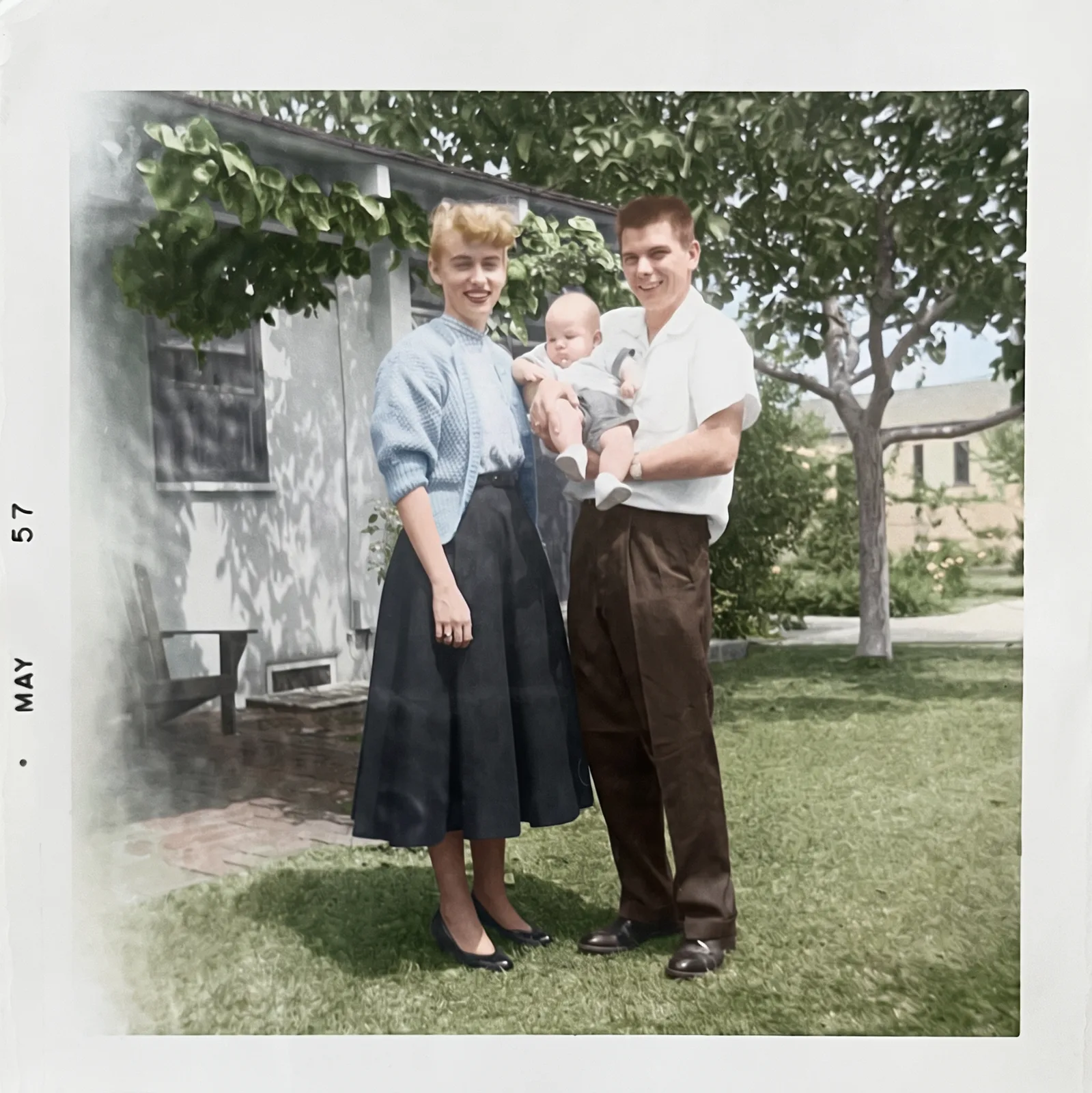Restored: A young couple holding their baby in a garden, May 1957